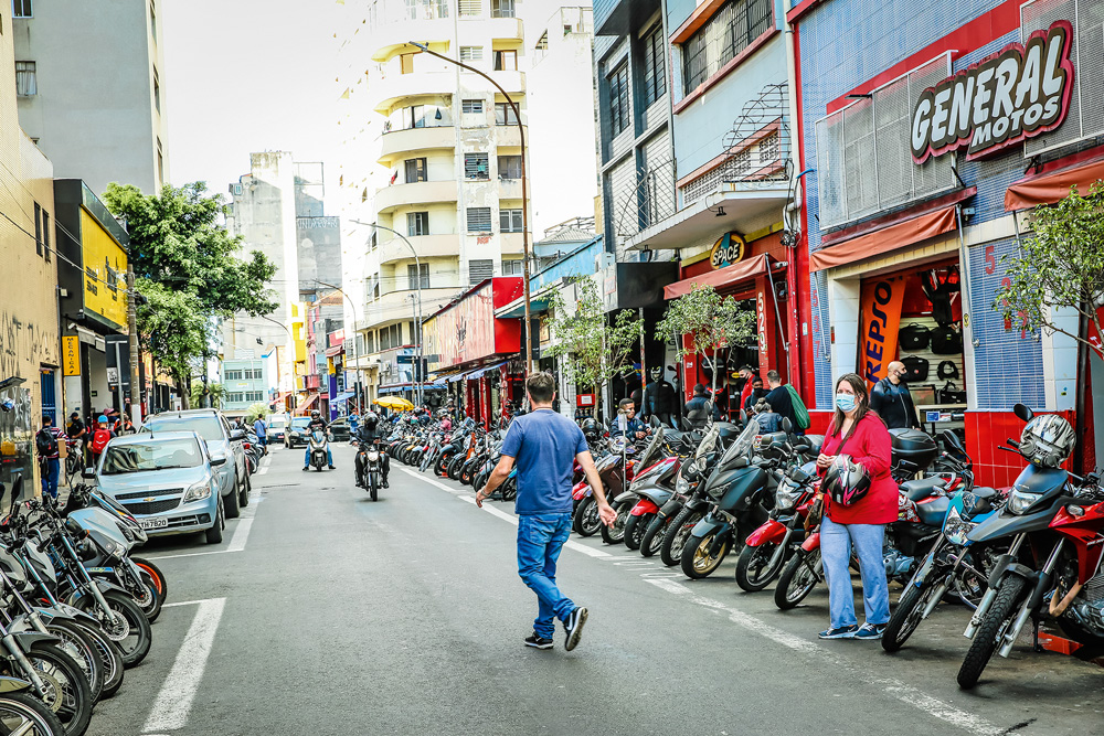 A imagem mostra a rua General Osório. Estreita, há muitas motos estacionadas no lado direito da imagem e um homem atravessando a rua.