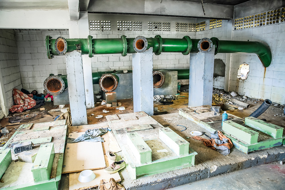 A imagem mostra uma pessoa deitada e com cobertas dentro da estação da Sabesp.