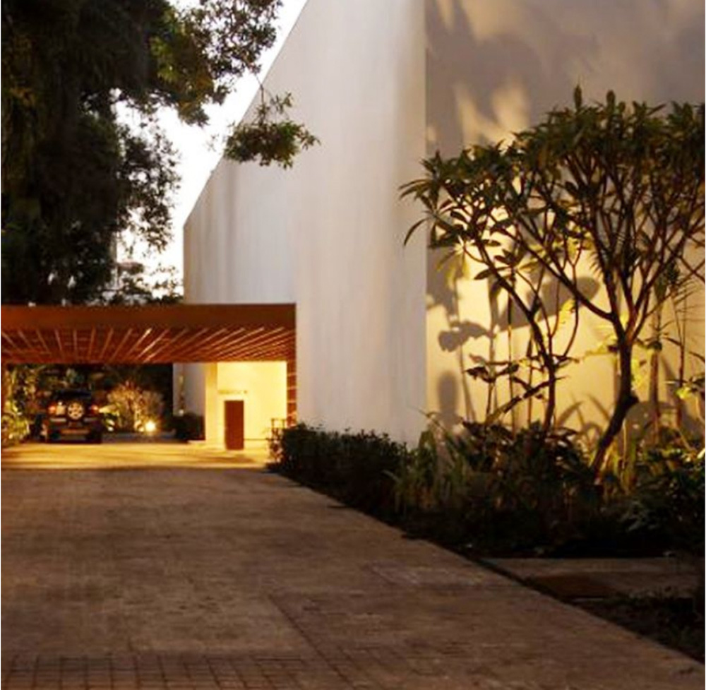 Casa Fasano Foto de um grande galpão pintado de branco com entrada e porta iluminada. Algumas árvores ao lado
