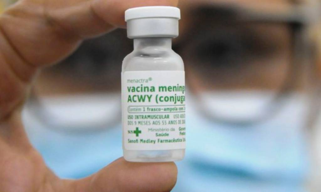 Frasco de Vacina de meningite aparece entre os dedos de uma pessoa.