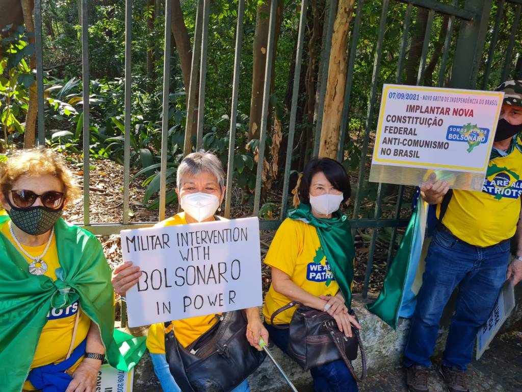 Imagem mostra três senhoras, uma dela segura um cartaz que diz: militar intervention with bolsonaro in power