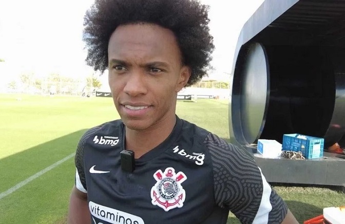 Imagem mostra jogar Willian sorrindo no gramado do centro de treinamento do Corinthians