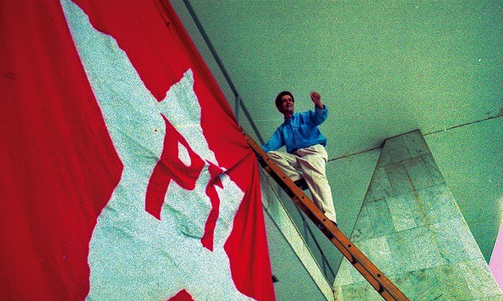 Imagem mostra Toninho do PT subindo em uma escada, com a bandeira do PT ao lado