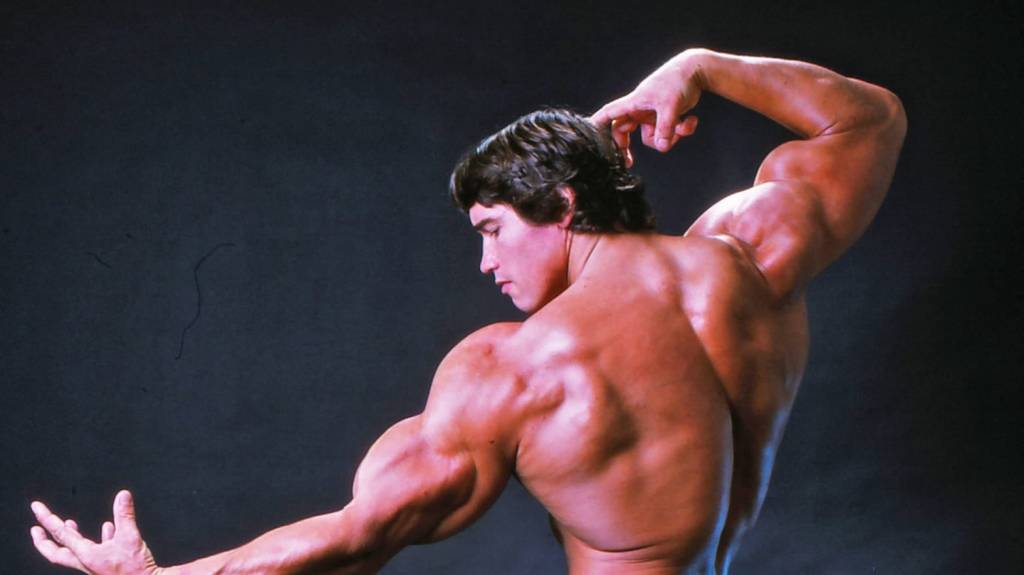 Arnold Schwarzenegger de costas fazendo pose com os músculos no filme 