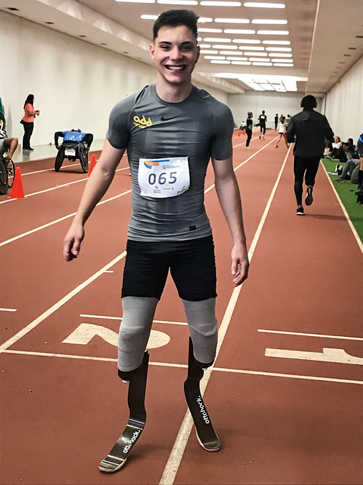 roger jacintho posando para a foto. ele está em uma pista de atletismo, com roupas esportivas. ele tem próteses nas duas pernas