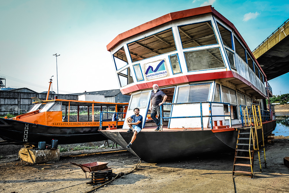 foto da frente do barco Almirante do Lago atracado no Cebolão, com um pouco de perspectiva de seu tamanho. Victor e Douglas aparecem pequenos na parte da frente do barco posando para a foto