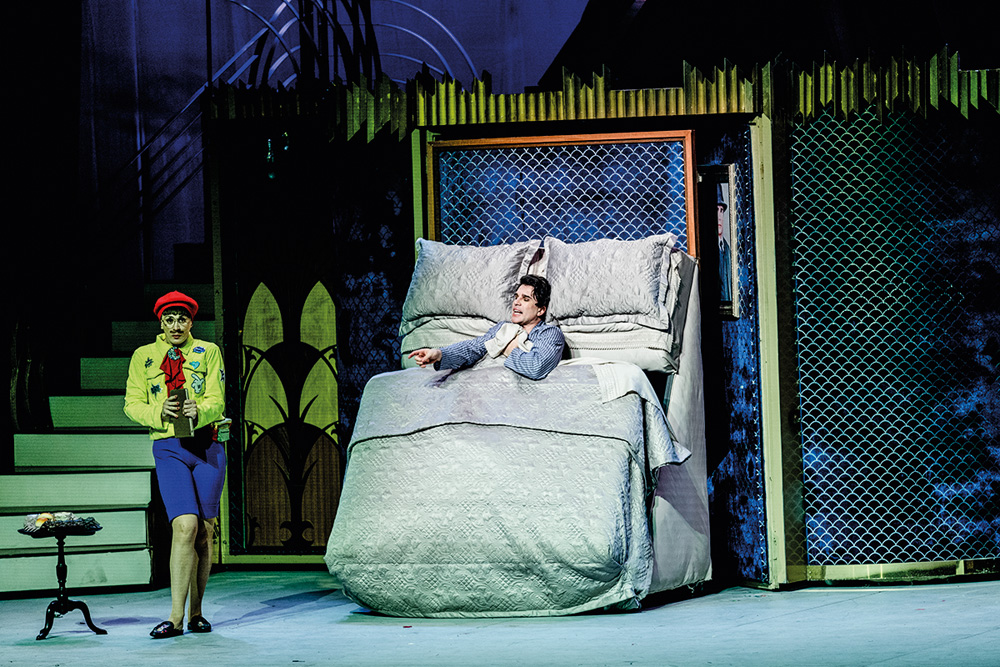 Em cena em um palco de teatro, Claudia Raia e Jarbas Homem de Mello dialogam. Ele está em uma cama que está na vertical, debaixo do cobertor. Ela, vestida de um menino, segura um livro