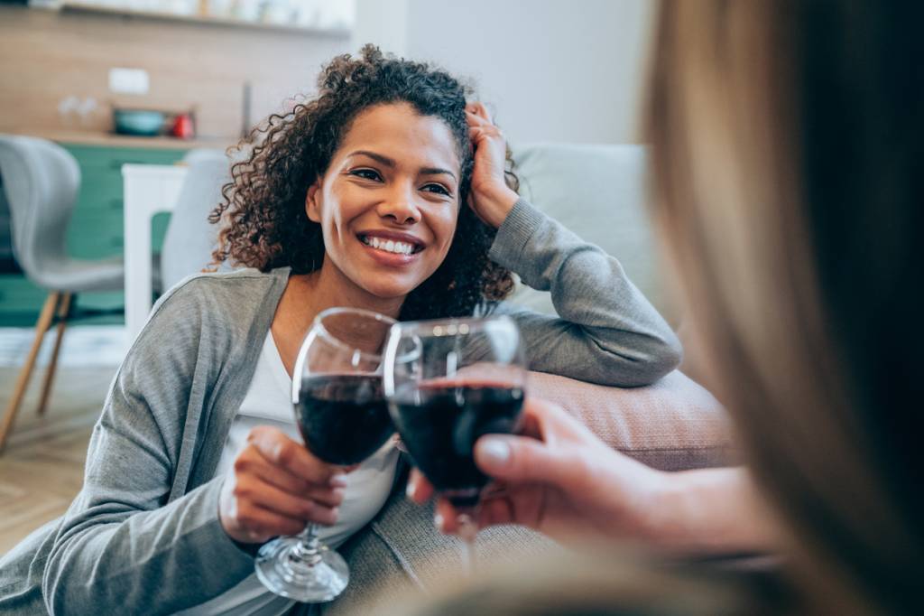 Duas mulheres bebem uma taça de vinho enquanto conversam sentadas no chão