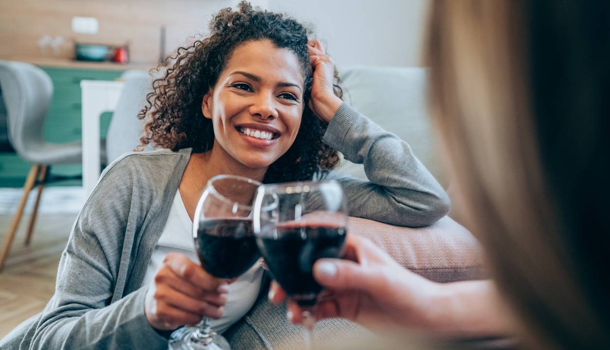 Duas mulheres bebem uma taça de vinho enquanto conversam sentadas no chão