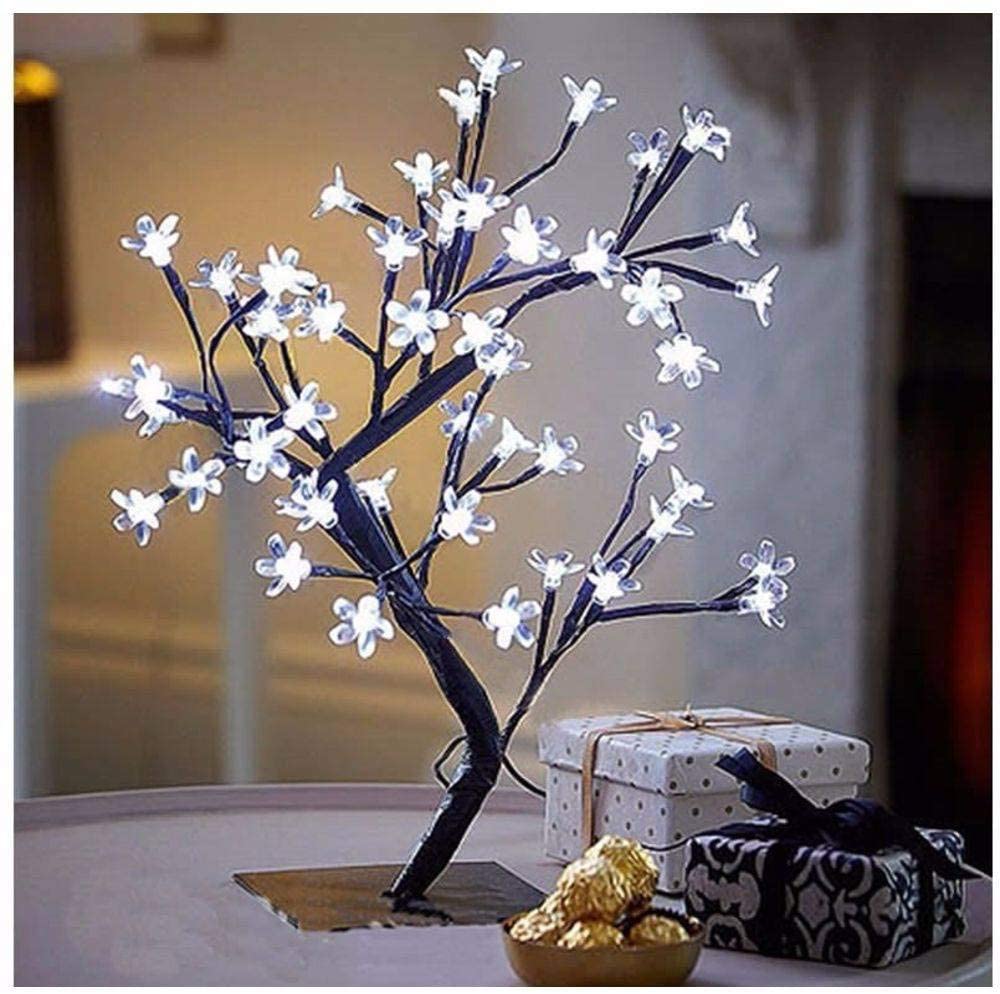 Uma luminária branca acesa em formato de árvore de cerejeira. Está em uma mesinha de canto ao lado de outros adornos