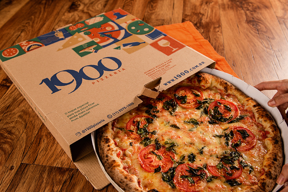 Pizza sabor margherita parcialmente dentro da caixa da pizzaria 1900
