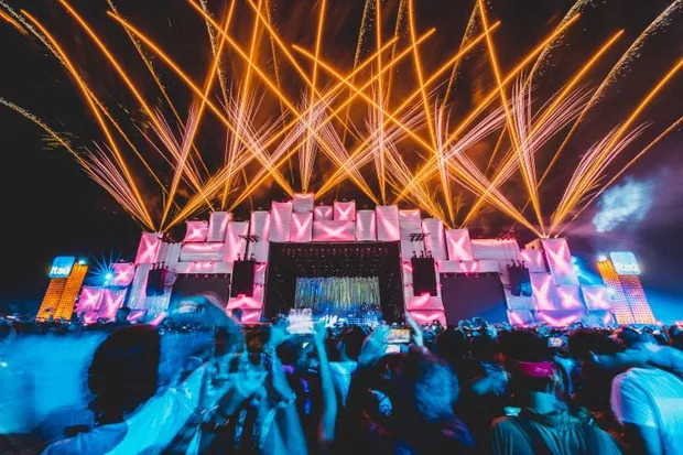 Imagem do Palco Mundo com holofotes iluminando céu escuro, com pessoas olhando para o palco no primeiro plano.