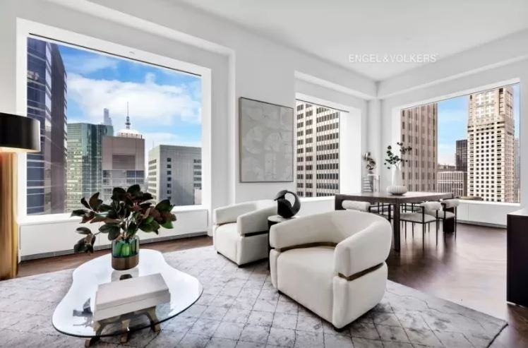 sala-de-estar-432-park-avenue-arranha-céu-milionário-manhattan-problemas-processo-judicial sala de estar ampla com diversos móveis claros e duas janelas grandes com vista para a cidade
