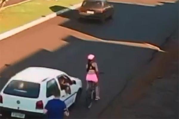 Imagem mostra frame de vídeo, em que aparece uma rua; carro se aproxima de mulher que anda de bicicleta na lateral da pista