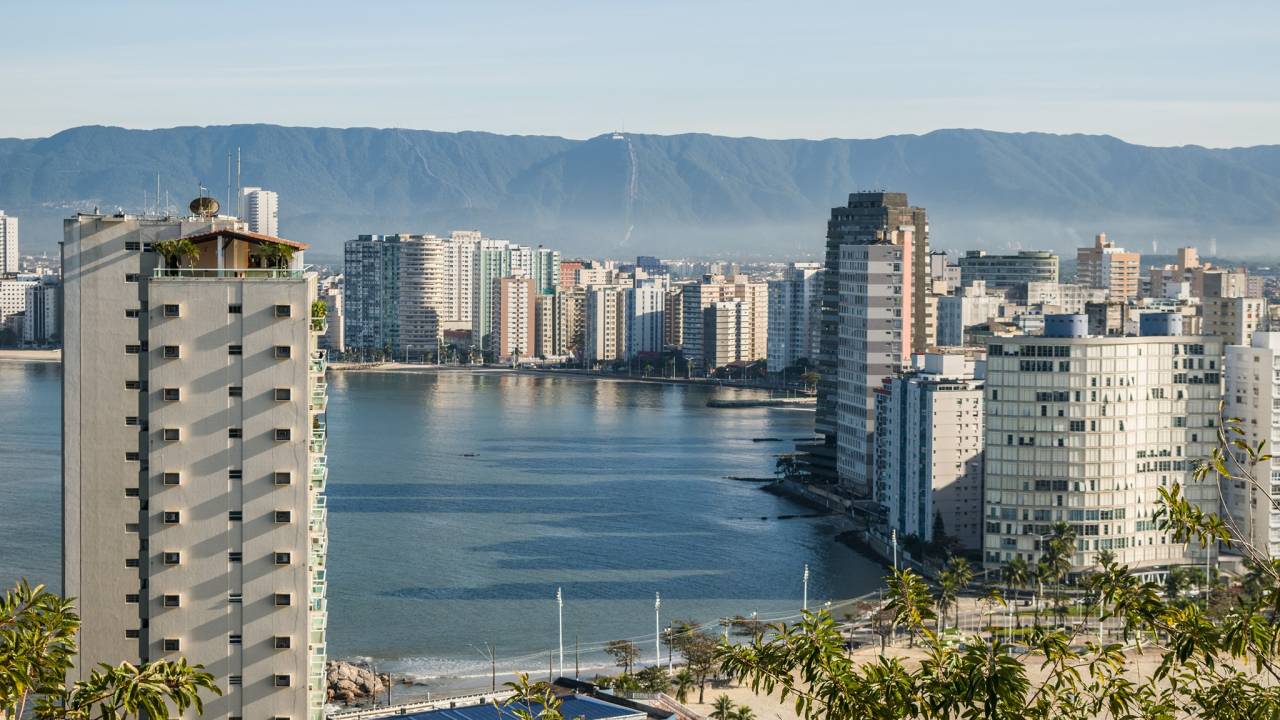 A foto mostra paisagem em São Vicente, com prédios e praia ao fundo