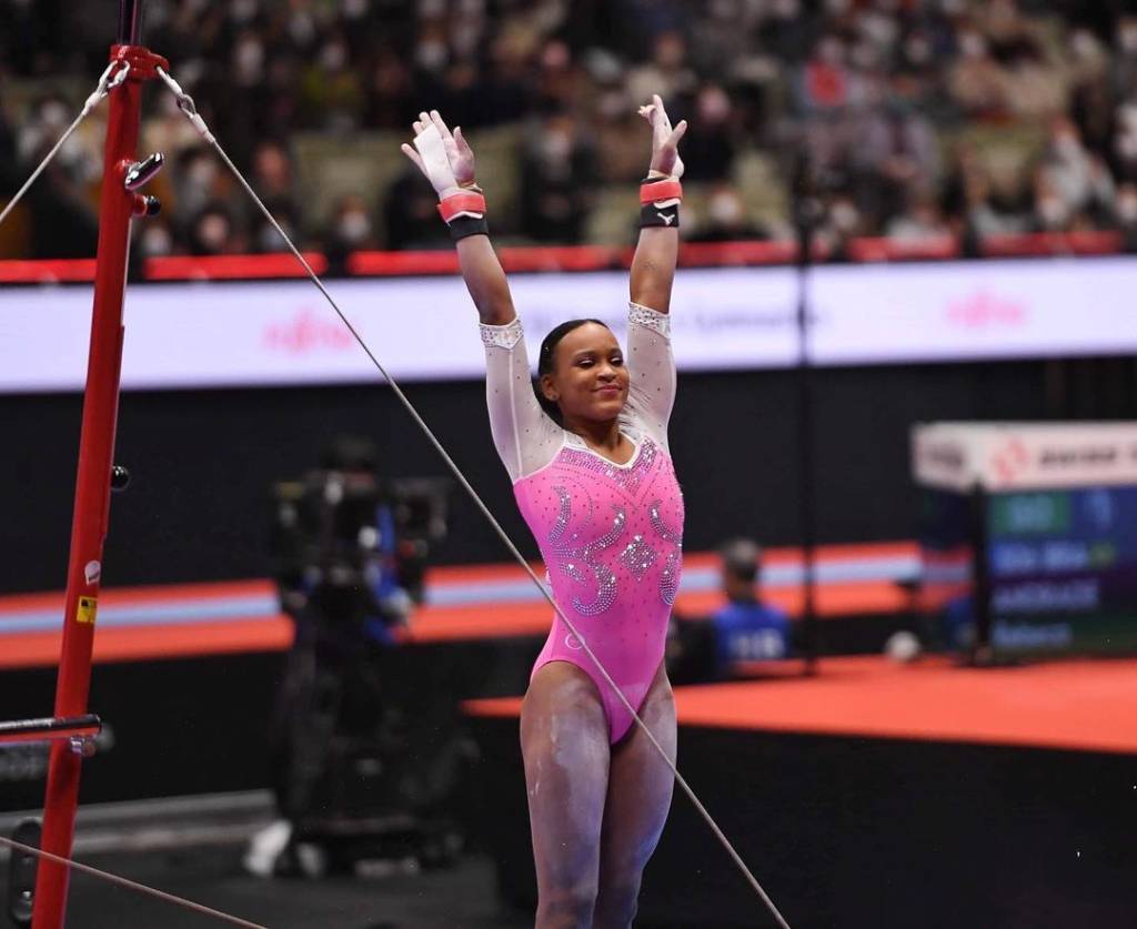 A atleta Rebeca Andrade de braços para cima após terminar apresentação nas barras assimétricas.