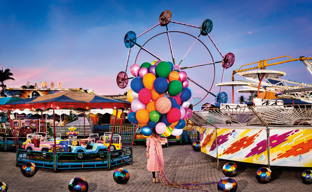 flávia junqueira em parque de diversões com núvem de balões, de diferentes cores, cobrindo de sua cintura para cima