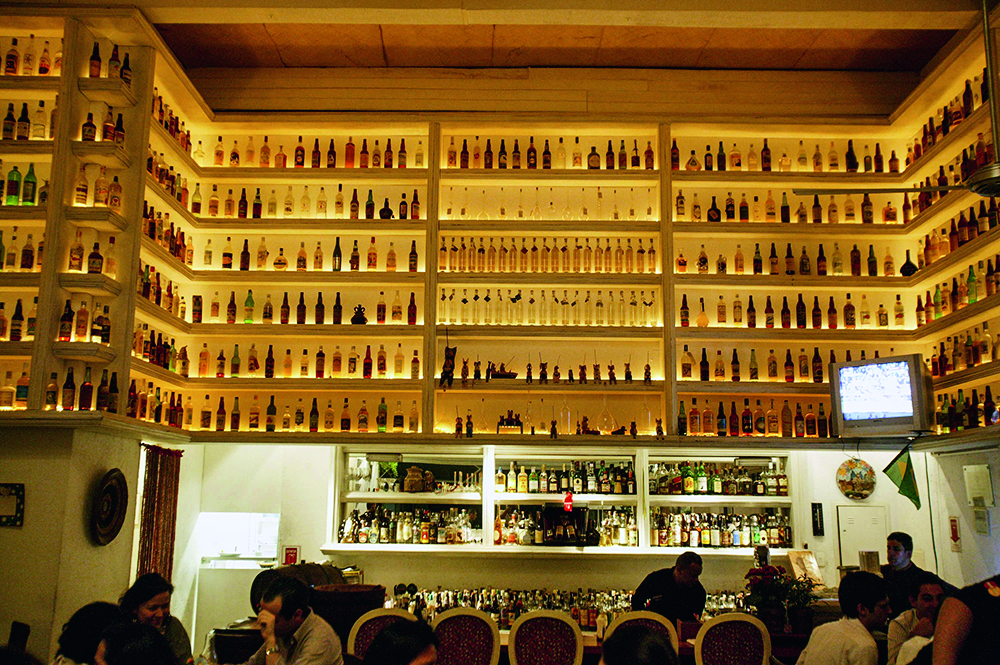 O bar Universidade da Cachaça com uma parede de prateleiras com garrafas da bebida ao fundo.
