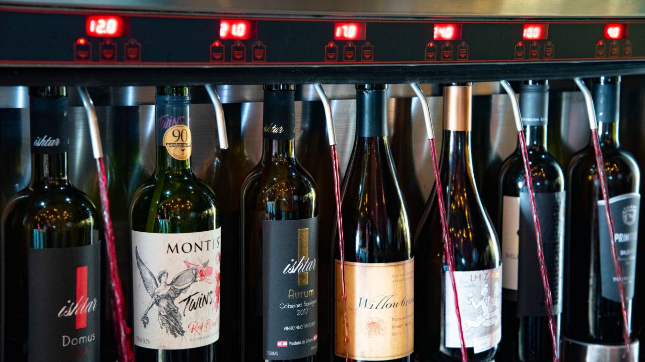 Garrafas de vinho acompladas à maquina com torneiras soltando vinhos tintos.