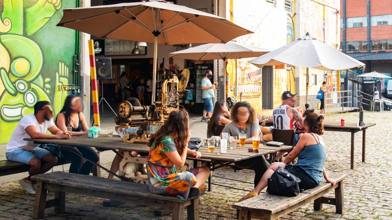 Espaço ao ar livre da Cervejaria Tarantino, com pessoas sentadas em mesa de madeira coberta por guarda-sóis.