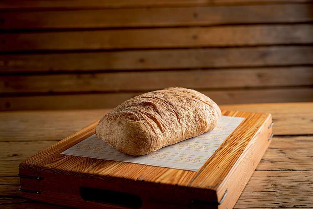 Pão do tipo ciabatta fotografado sobre uma tábua de madeira sobre uma mesa