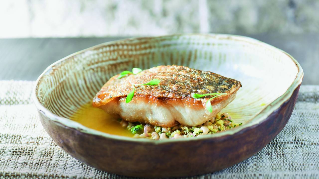 Prato fundo com posta de peixe dourada sobre salada de feijão-manteguinha.