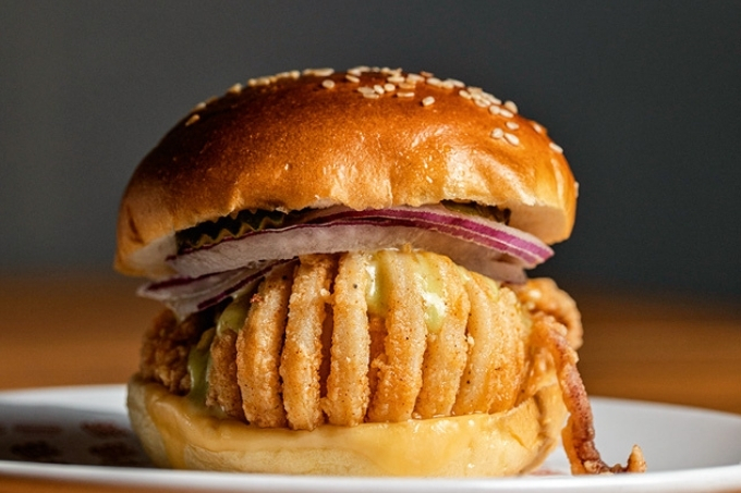 Pão de hambúrguer com gergelim, fatias de cebola roxa e lula compõem o sanduíche da foto