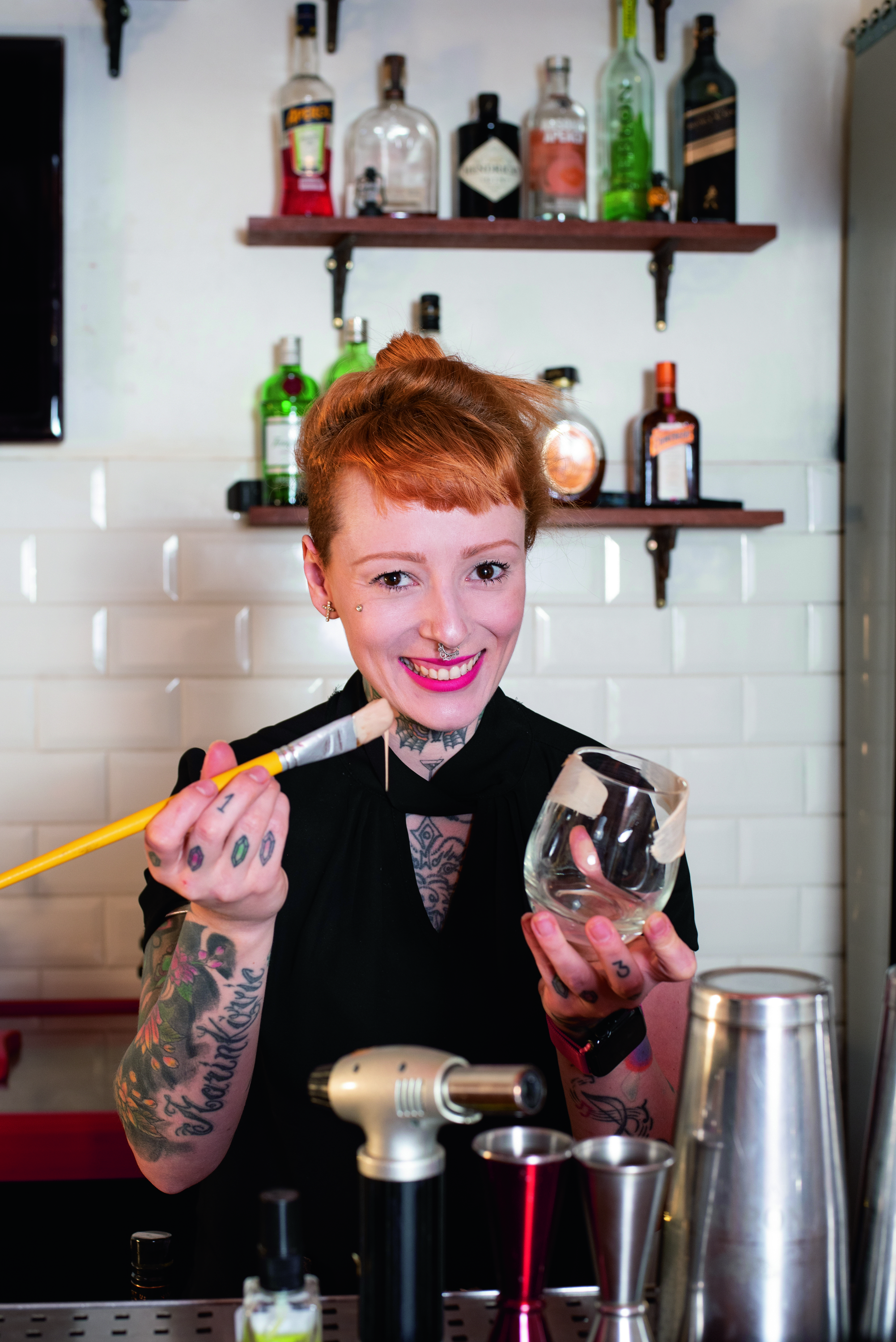 A bartender Stephanie Marinkovic, de cabelo ruivo e braços tatuados, pintando o lado de fora de um copo com ganache de chocolate branco.