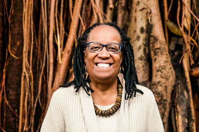 sueli carneiro sorrindo para a câmera à frente de grandes raízes de árvore