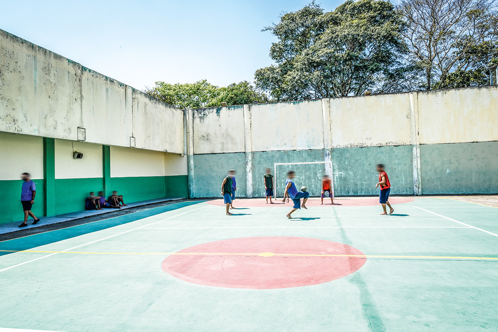 A imagem mostra jovens jogando futsal em uma quadra dentro da Fundação Casa.
