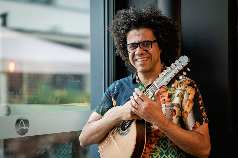 Hamilton de Holanda por Fernanda Nigro 4.jpg A imagem mostra Hamilton sorrindo, segurando seu instrumento, apoiado em uma janela.