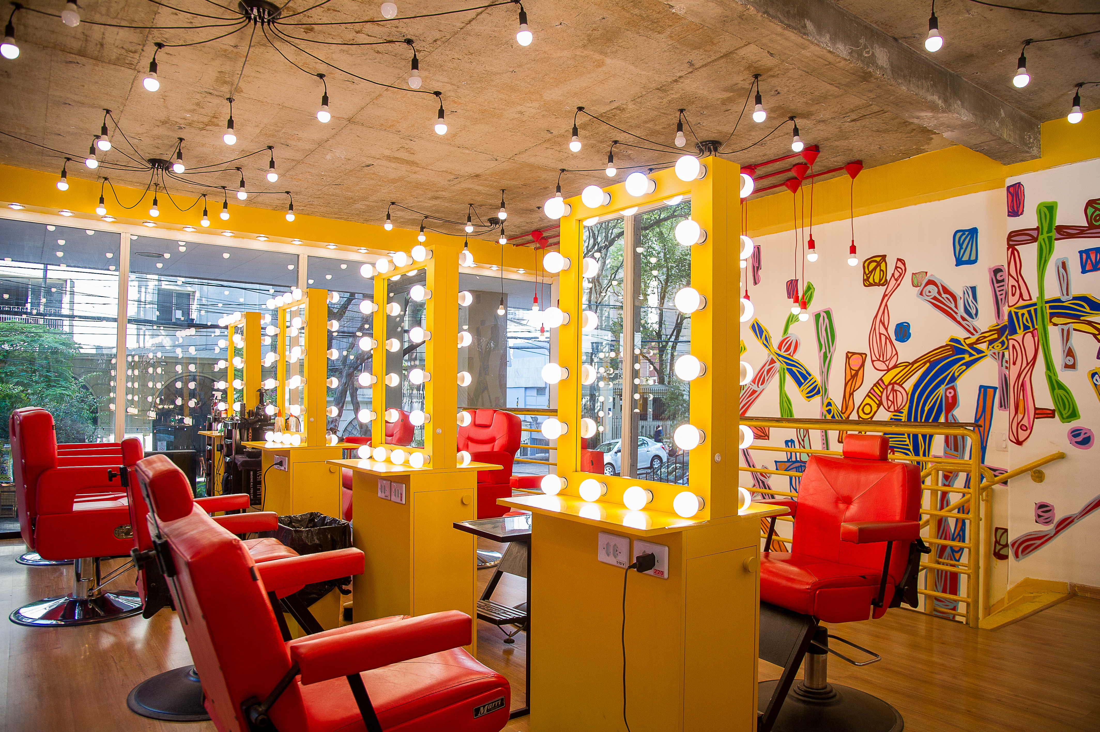 Cadeiras vermelhas e espelhos iluminados de salão aparecem na diagonal.