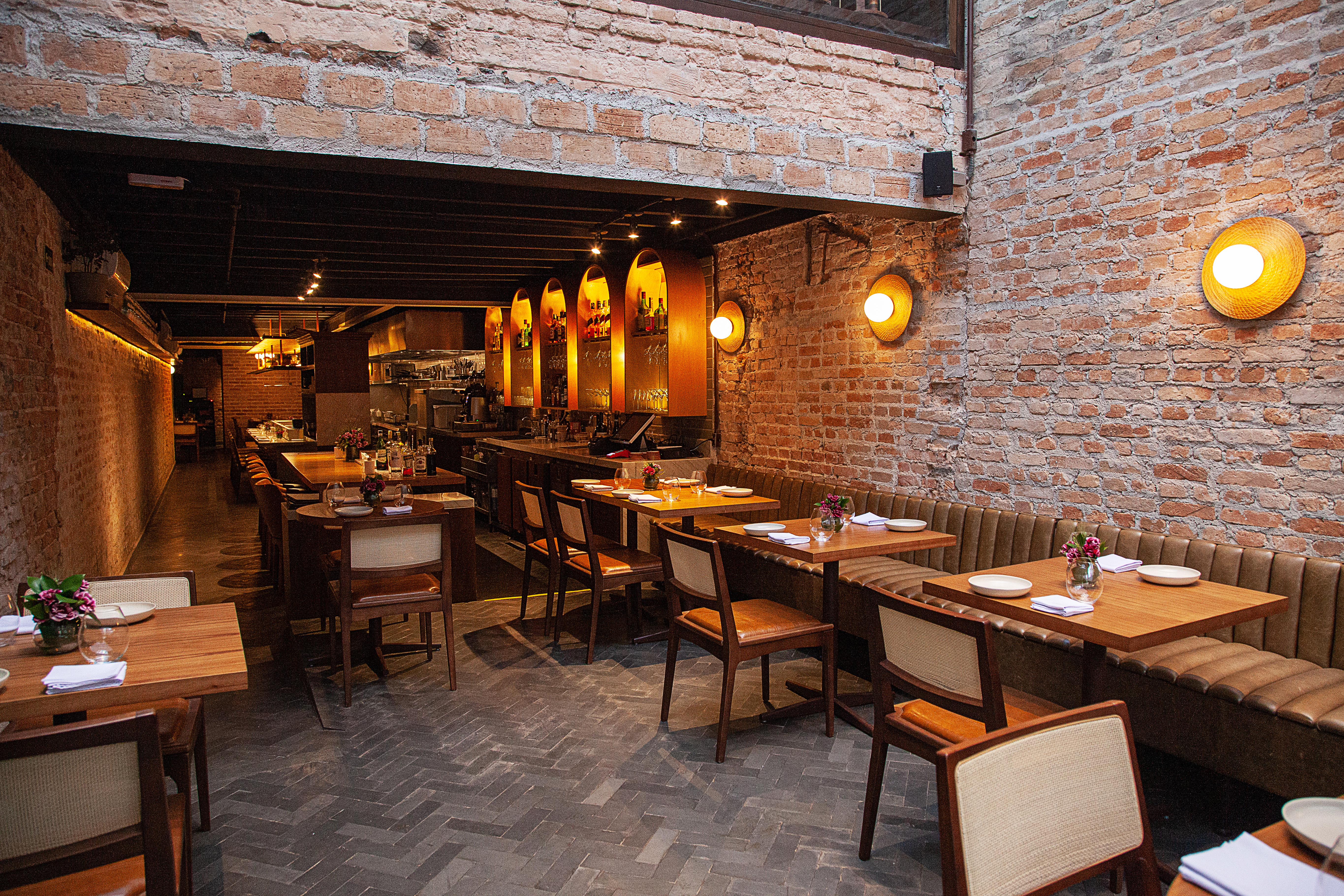 Salão do restaurante Nelita, com paredes de tijolinhos, mesas de madeira que se estendem até o fundo na lateral esquerda.