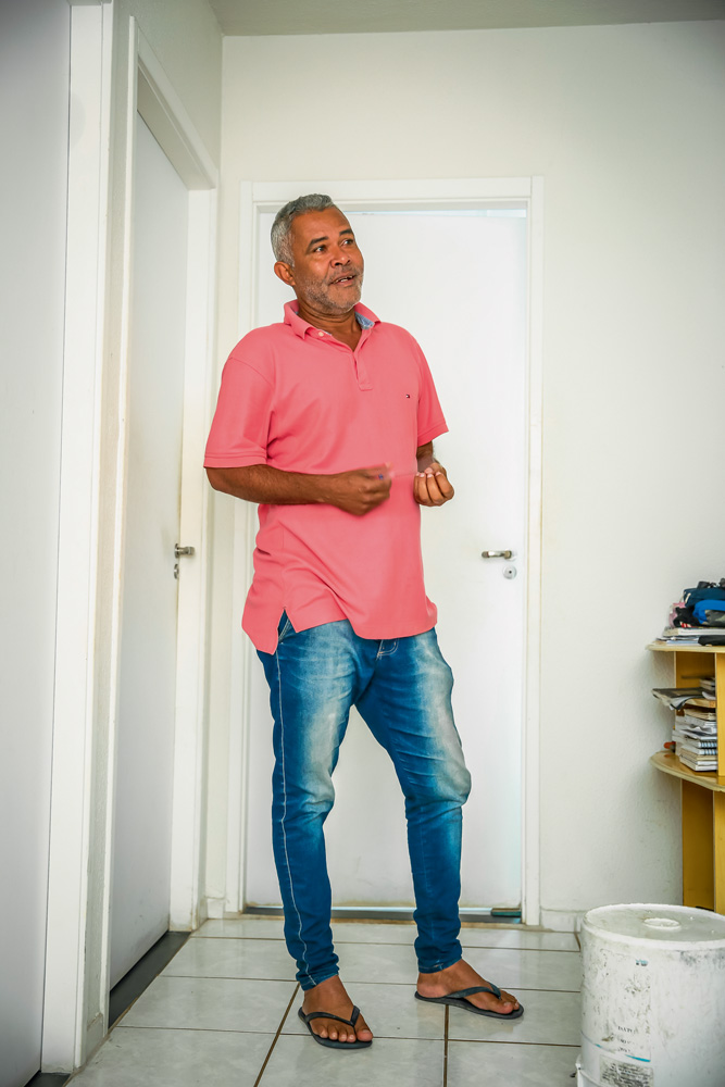 Um homem negro grisalho está gesticulando e conversando em um apartamento branco