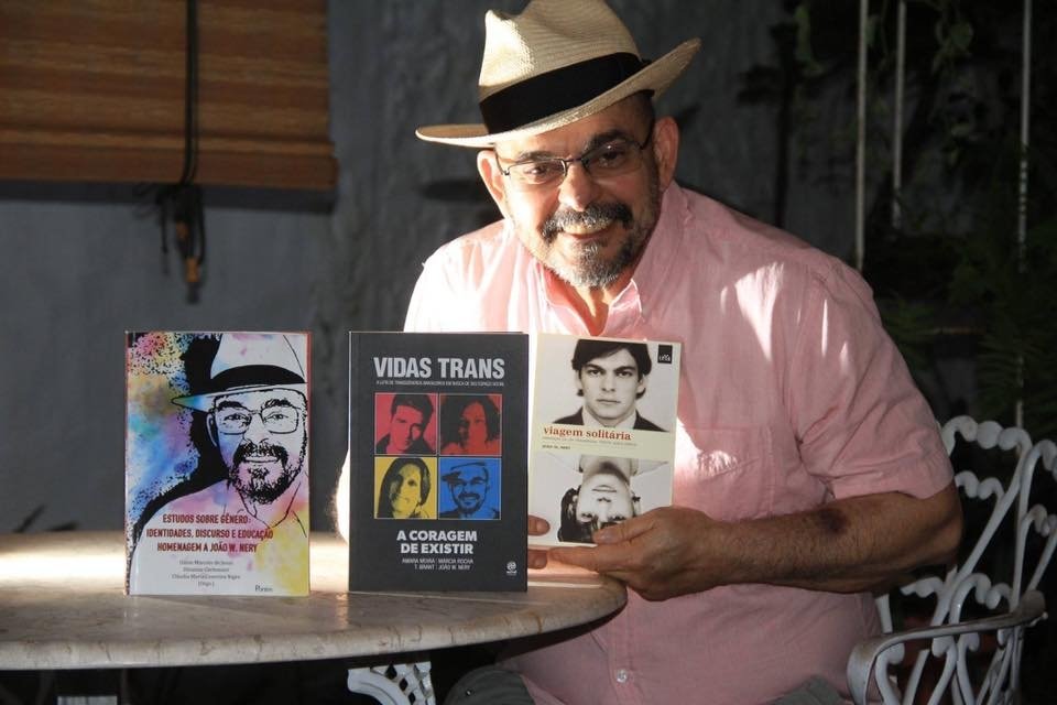 A imagem mostra João Nery, sentado em frente à uma mesa, com três livros em sua frente.