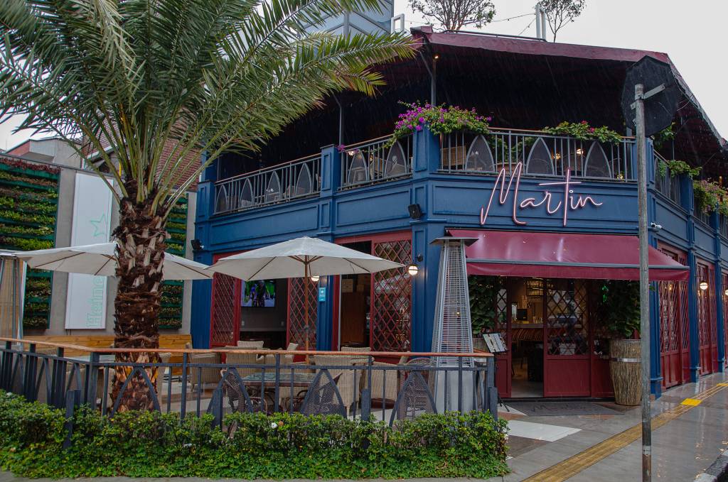 Fachada do Martin Bar. Casa pintada de azul e vermelho com mesas ao ar livre em varanda na parte da frente.