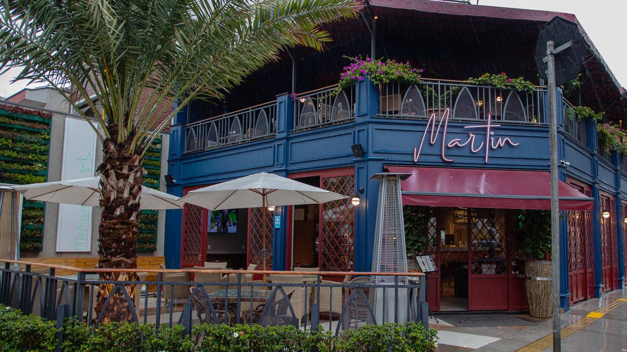 Fachada do Martin Bar. Casa pintada de azul e vermelho com mesas ao ar livre em varanda na parte da frente.