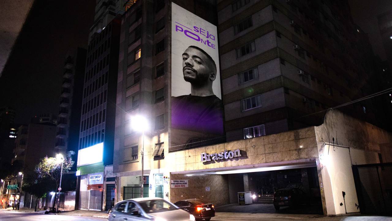 Imagem mostra rua Augusta à noite com projeção em um prédio mostrando o rosto de um jovem negro.