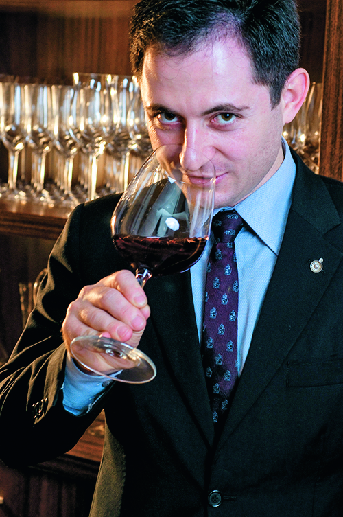 Tiago Locatelli de terno sentido o aroma de um vinho tinto na taça.