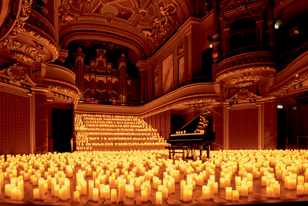 A foto mostra um grande espaço cheio de velas no chão e em uma escadaria larga em frente. Há um piado de calda, com algumas velas em cima no centro do salão.