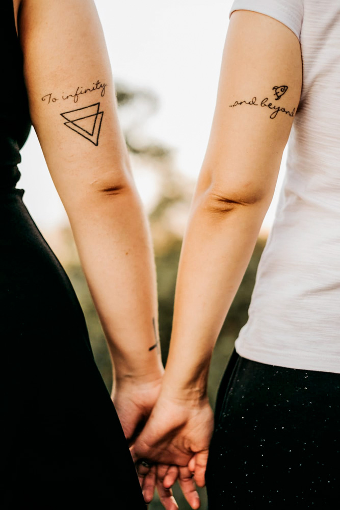 casal-lésbico-carolina-thais-adoção-nosso-louco-amor-maos-dadas.jpg braços de caroline e thais. elas estão de mãos dadas e é possível ver que cada uma possui uma tatuagem sobre o filme toy story na região acima do cotovelo