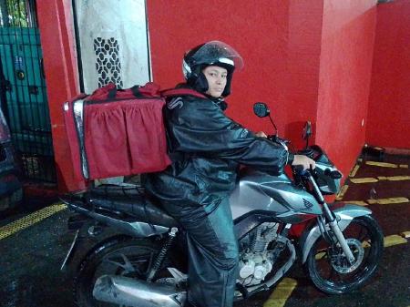 Imagem mostra mulher em cima de moto com mochila de entrega de comida