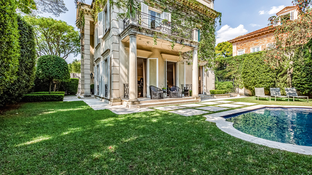 vista do jardim de casa com trepadeiras nas paredes. no jardim, há muito espaço de grama verde e uma piscina, à direita