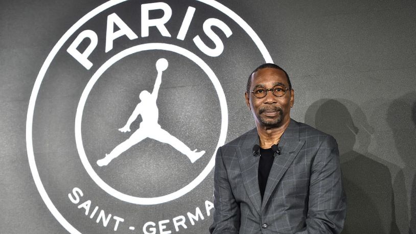 Imagem mostra homem de terno e óculos na frente de logotipo do time Paris Saint-Germain