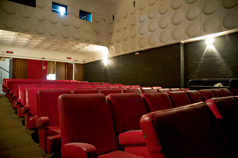sala do cine bijou, com cadeiras vermelhas, parte de cima das paredes branca com relevos circulares e sala de projeção na parte de cima
