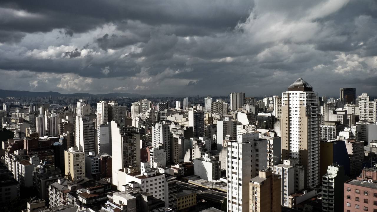 Foto tirada do topo de um prédio mostra diversos prédios em São Paulo e um céu extremamente nublado e escuro.