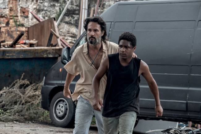 A imagem mostra Rodrigo Santoro e Christian Malheiro correndo em uma rua durante o filme 7 Prisioneiros