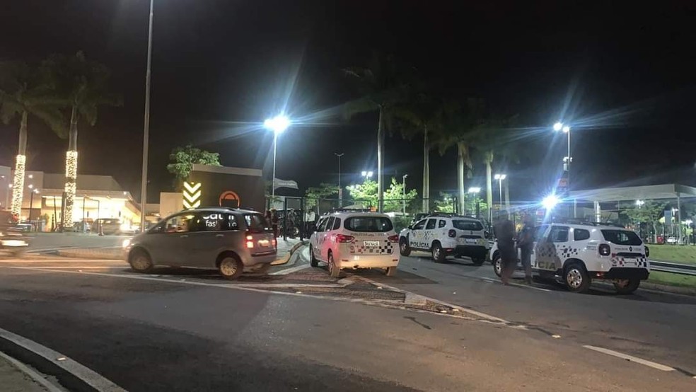 Imagem mostra carros da polícia em rua, com um estabelecimento iluminado ao fundo.