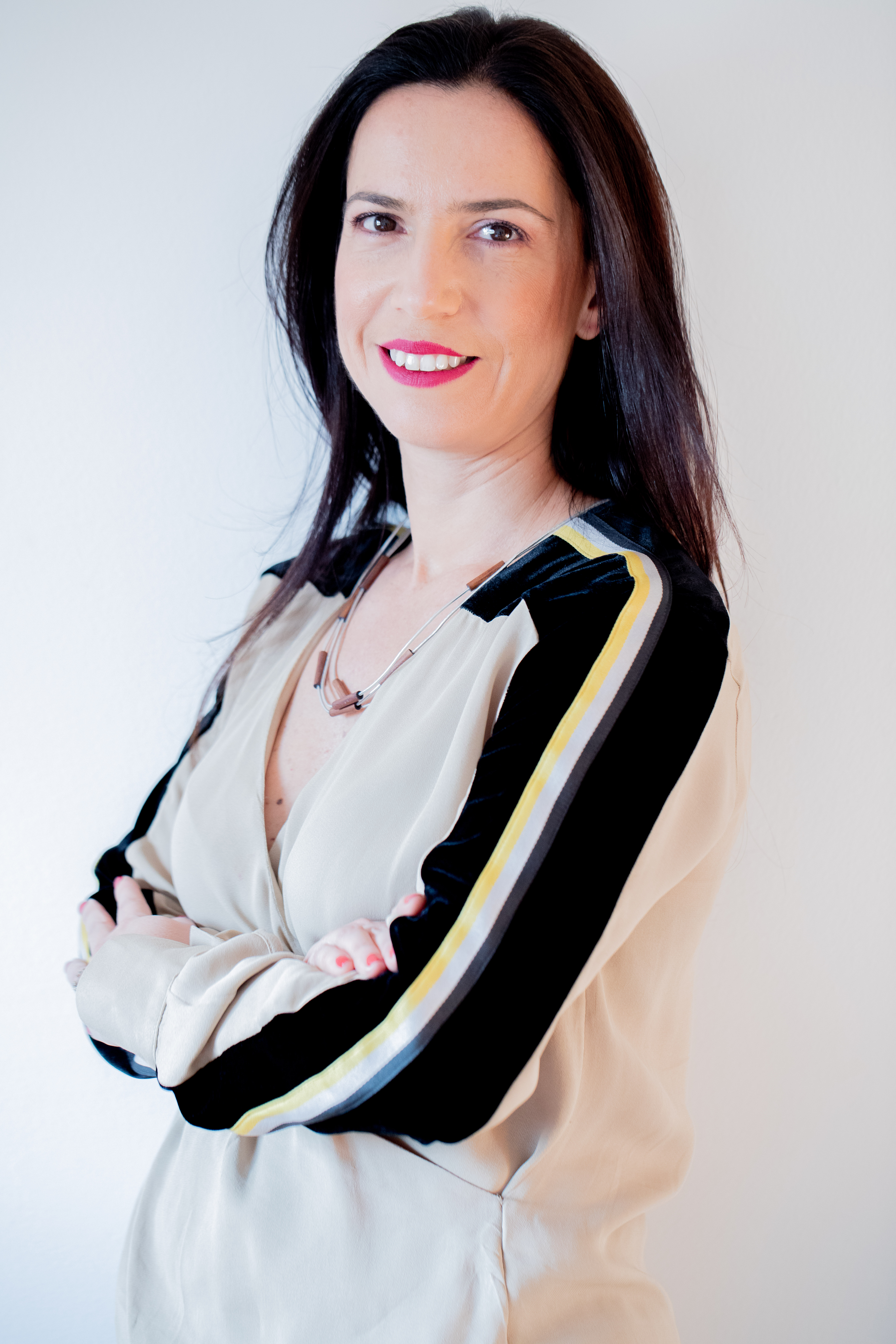 A fonoaudióloga Alessandra Scavone posa de braços cruzados e sorrindo. veste roupa com mangas pretas e tecido branco.