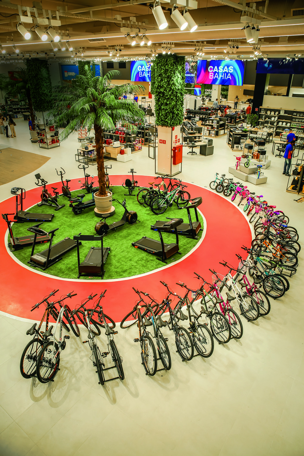 Foto tirada de um plano alto, mostra um gramado sintético em formato circular, rodeado por uma pista de corrida vermelha e por inúmeras bicicletas.